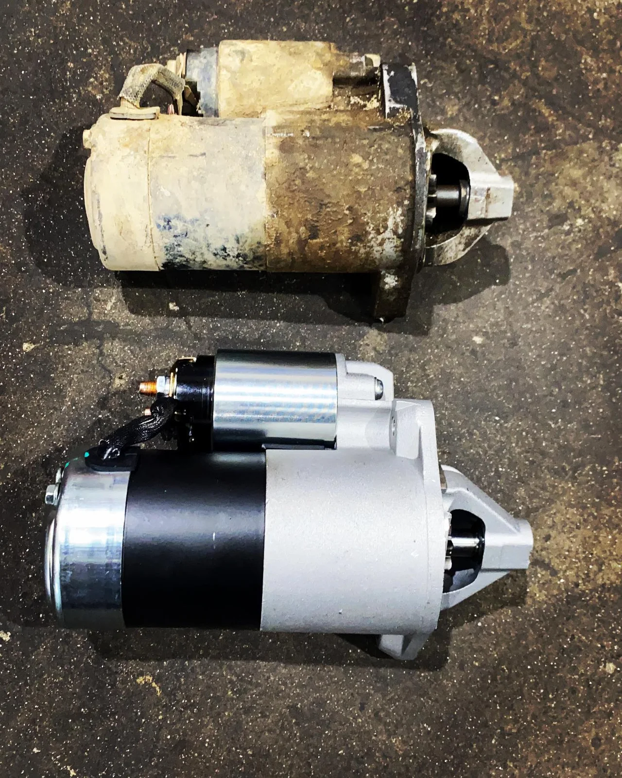 Old and replacement starter motors compared on a workbench